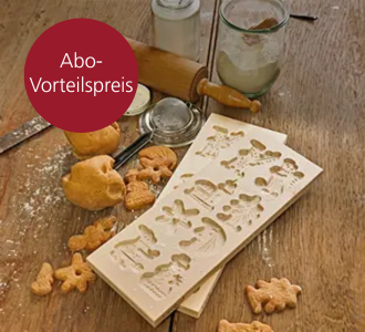 Eine Holzform in die acht weihnachtliche Motive reingeritzt worden sind. Auf der Holztischplatte darunter liegen weitere Backutensilien, Keksteig und Spekulatiuskekse.