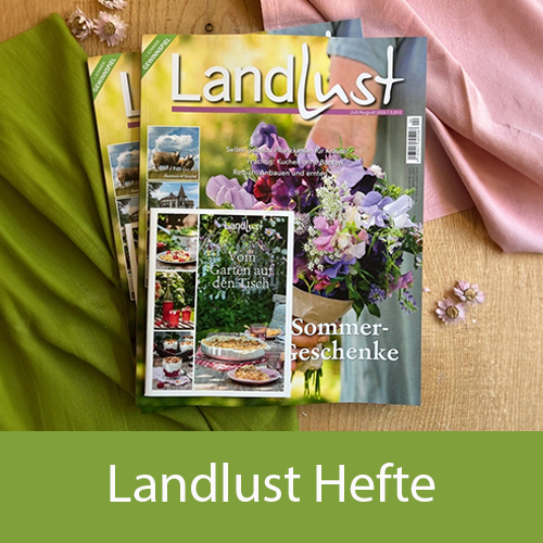 Zwei &bdquo;Landlust&ldquo;-Magazine liegen auf einem hellen Untergrund, umgeben von unterschiedlichen Stoffen und kleinen rosa Bl&uuml;ten. Bild verlinkt zu dem neuen Landlust Heft.