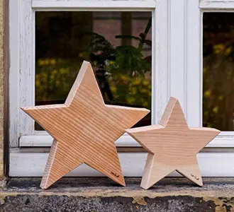 Zwei unterschiedlich große Sterne aus massivem Holz stehen auf der Fensterbank eines Hauses.