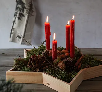 Ein Holztablett in Form eines fünfzackigen Sternes ist mit vier roten Kerzen, Tannengrün und Nüssen dekoriert.
