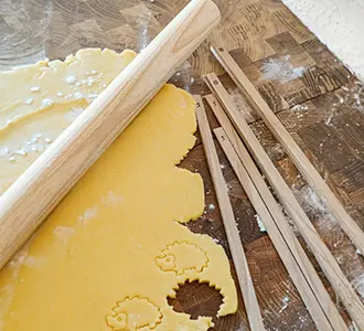Auf einer bemehlten Arbeitsplatte liegt eine Teigrolle aus Holz, mehrere Holz-Teigstäbe und ausgerollter Teig.