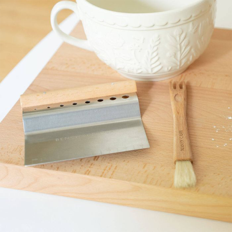 Auf einer Holzplatte liegt ein Holzpinsel und ein Teigschneider mit einem Metallschneider