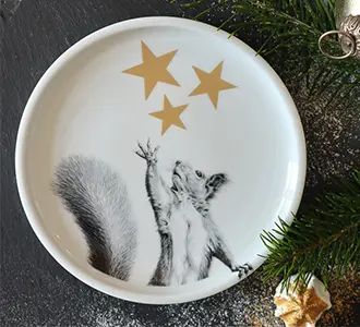 Ein weißer Teller auf dem ein Eichhörnchen in schwarz-weiß gezeichnet wurde. Auch goldene Sterne befinden sich darauf.