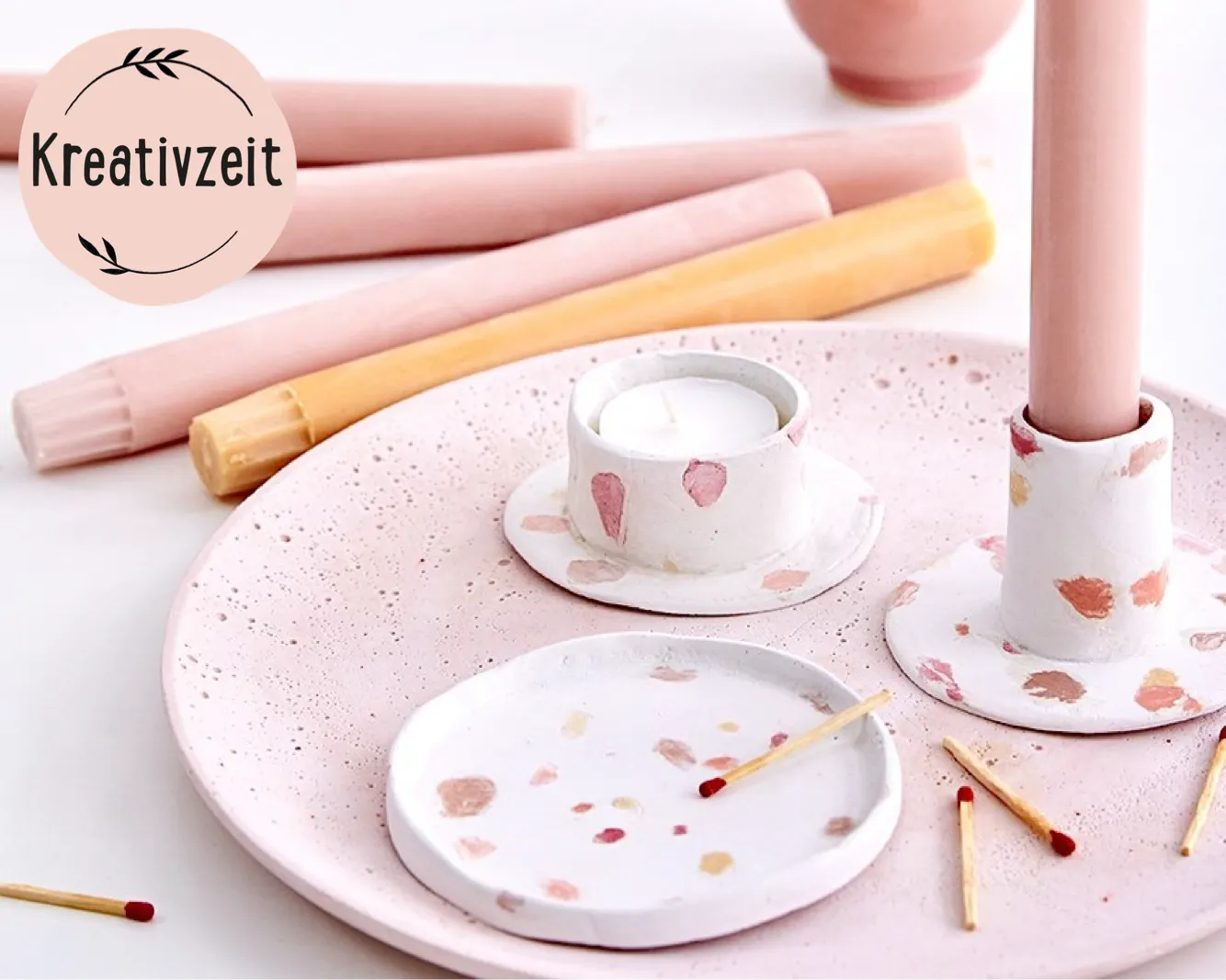 Rosa Kerzenteller mit Teelicht, hohen Kerzen und Streichhölzern dekoriert. Kreativzeit-Logo oben links. Bild verlinkt zum Workshop.