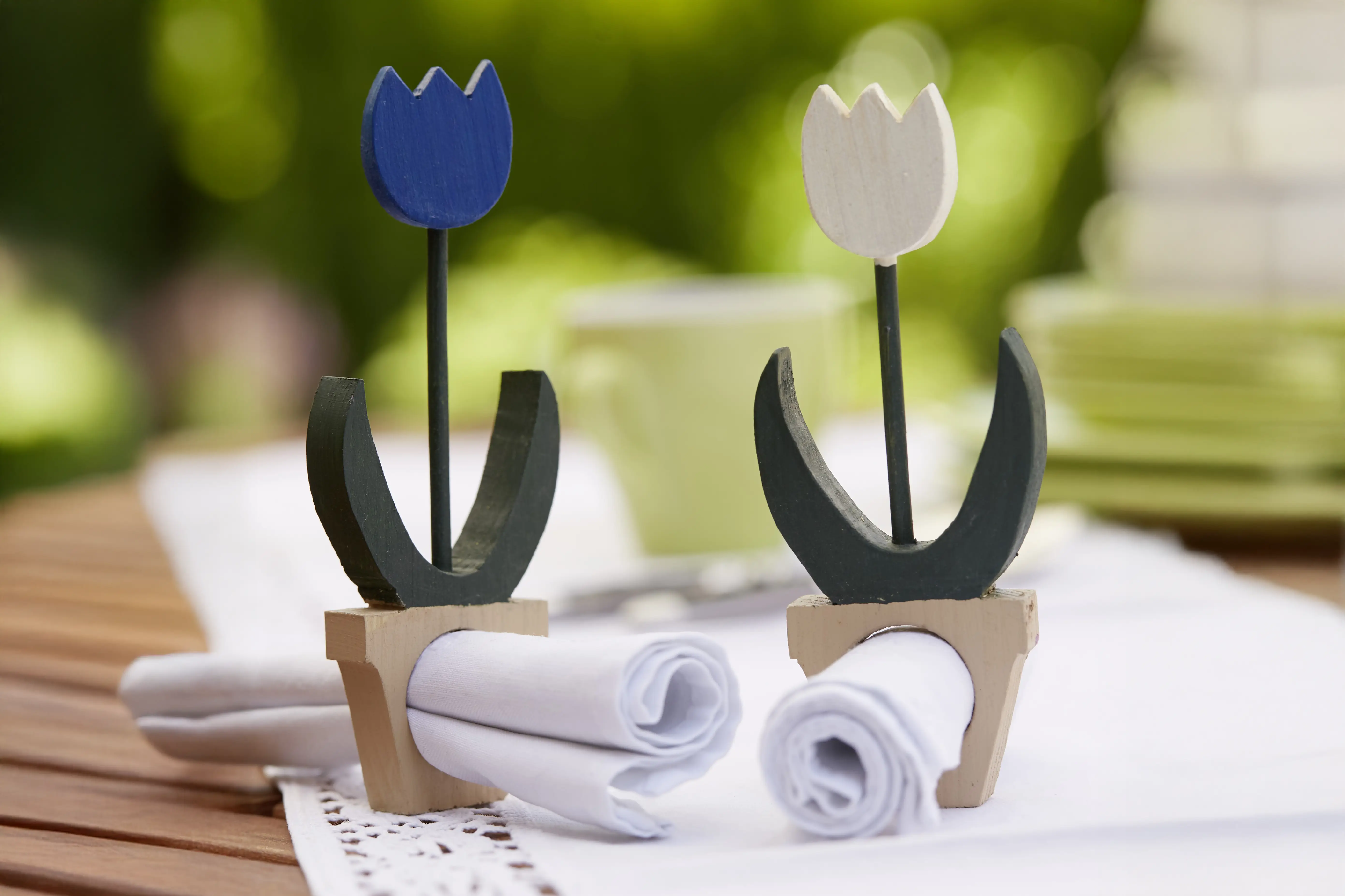 Tulpen aus Holz mit einem Blumetopf stehen auf einem gedeckten Tisch. Im Blumentopf ist ein Loch in dem Servietten stecken.