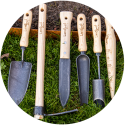 Verschiedene Landlust Gartenwerkzeuge liegen auf einem Rasen, angelehnt an einen Beetrand.