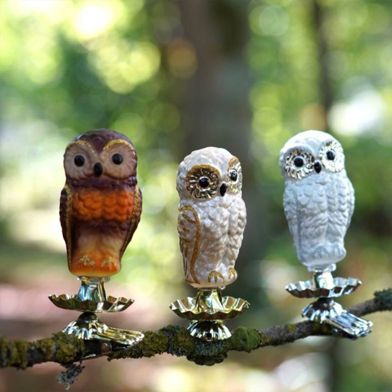 Drei Tannenbaumschmuck-Figuren in Form von Eulen sind auf einem Zweig befestigt. Die Eulen sind in weiß und braun Tönen gefärbt.