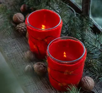 Zwei kleine Gläser mit einem Mantel von rotem Filz stehen auf einer Holzfensterbank. Daneben liegen Nüsse und Tannenzweige.
