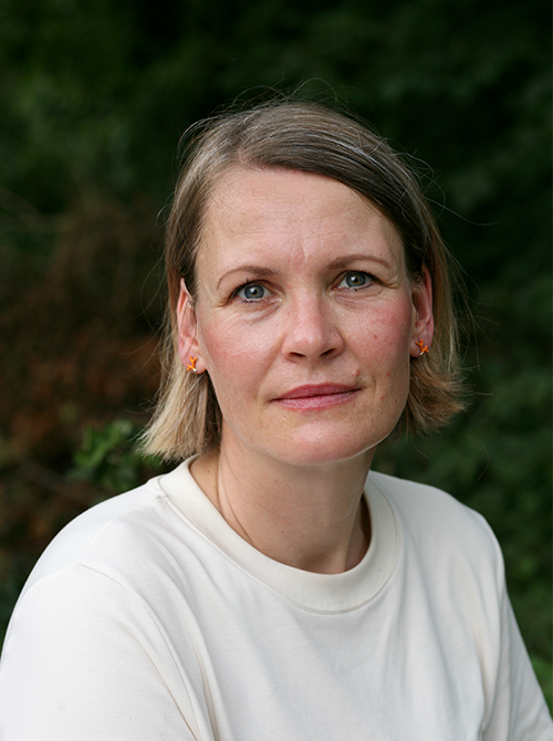 Eine Frau mit schulterlangen blonden Haaren und weißem T-Shirt schaut in die Kamera