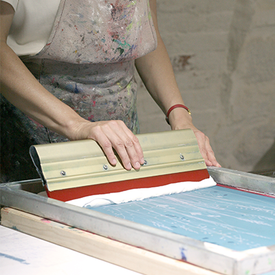 Eine Person verteilt Farbe auf einer Siebdruckform