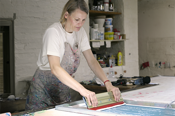 Eine Person macht Siebdruck. Sie verteilt gerade Farbe auf einem belichteten Sieb.