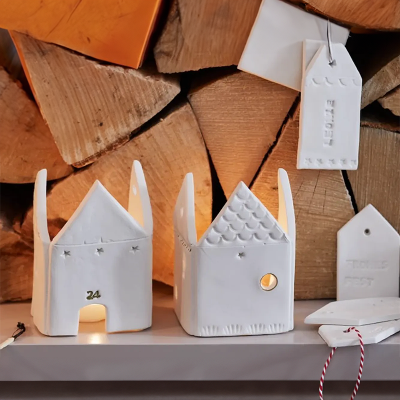 Aus FIMO-Modelliermasse geformte Häuschen stehen vor einer Holzwand.