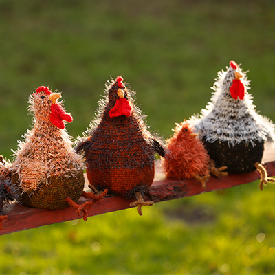 Gestrickte und gehäckelte Hühner sitzen auf einem Holzbrett im grünen