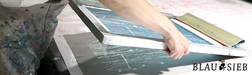 Eine Person macht Siebdruck. Sie ist dabei ein belichtetes Sieb auf eine Unterlage zu legen