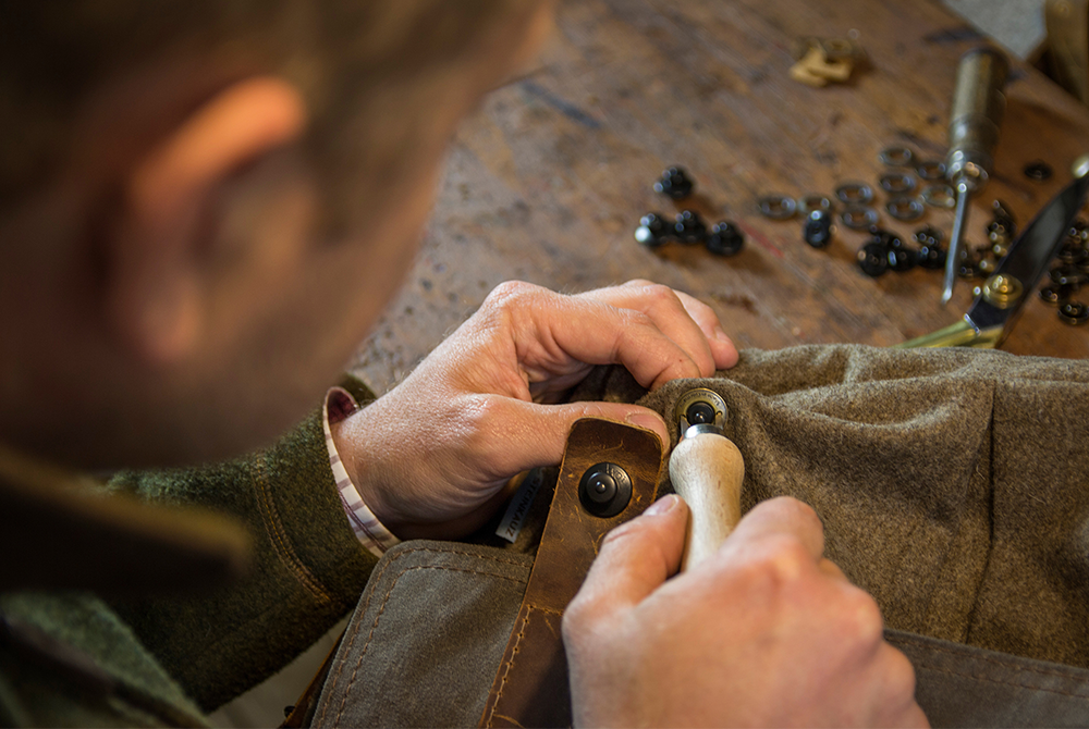 Eine Person befestigt Knöpfe an einem Kleidungsstück aus grünem Filz. Die Person arbeitet auf einem Holztisch
