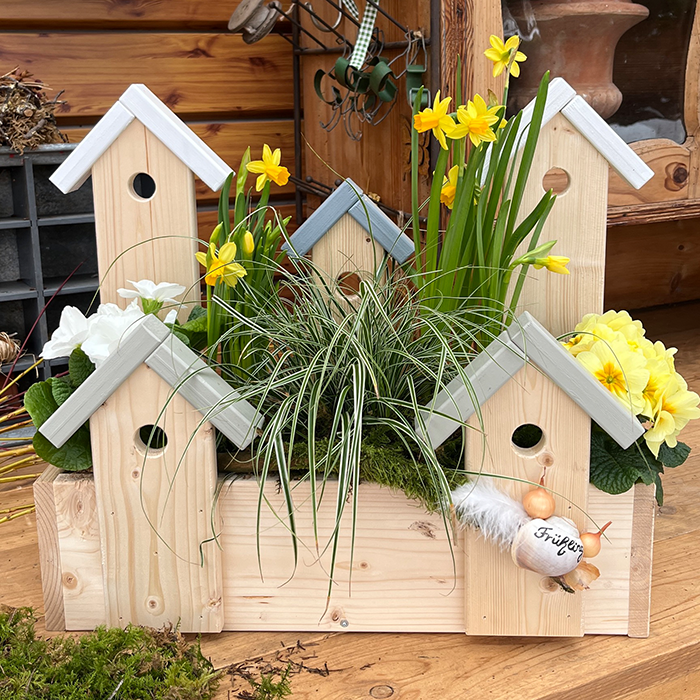 Holz Blumenkasten mit hellen Vogelhausformen, bepflanzt mit gelben und wei&szlig;en Blumen, gr&uuml;nes Gras, nat&uuml;rliche Holztextur, fr&uuml;hlingshaftes Arrangement.