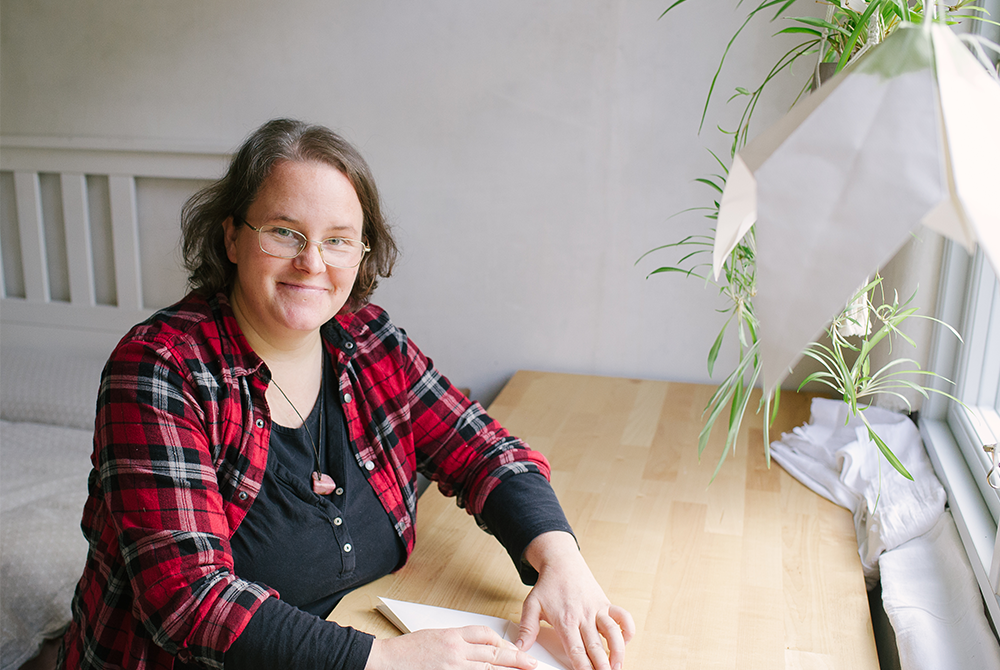 Eine Frau sitzt an einem Schreibtisch und faltet ein Papier